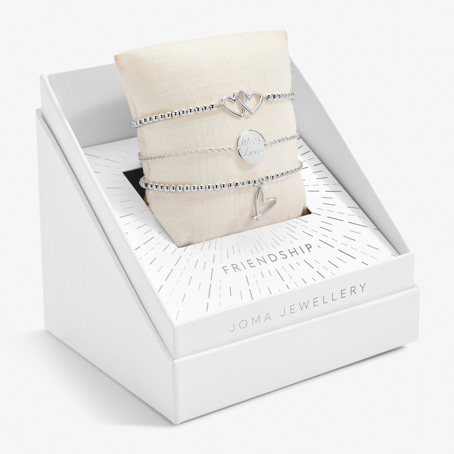 A white gift box with 'Joma Jewellery' branding containing three silver-plated bracelets with heart charms on a plush pillow.