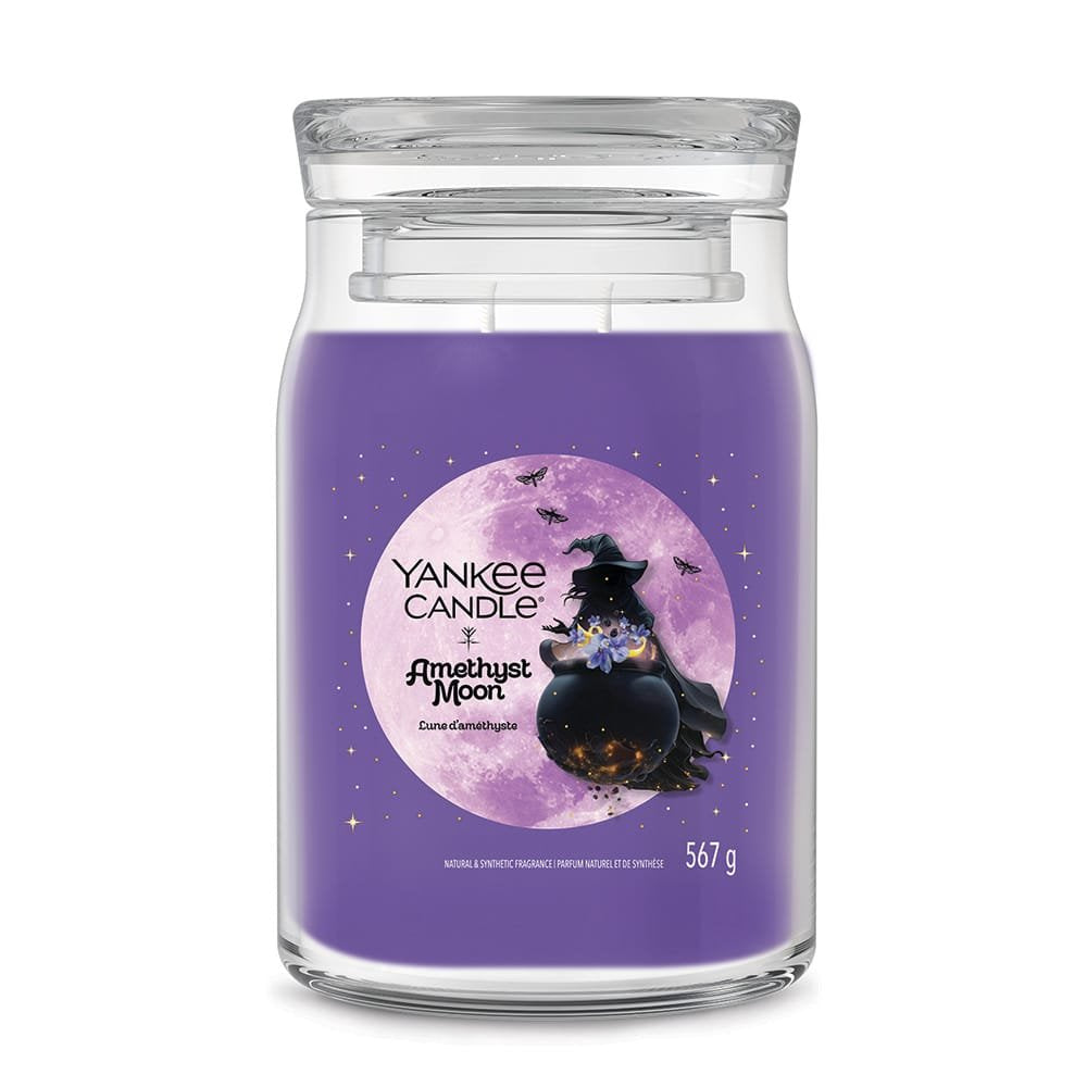 A Yankee Candle jar candle in a clear glass jar with a purple wax fill and a front label reading 'Yankee Candle x Amethyst Moon.' The label shows a witch, cauldron, moon, and stars.