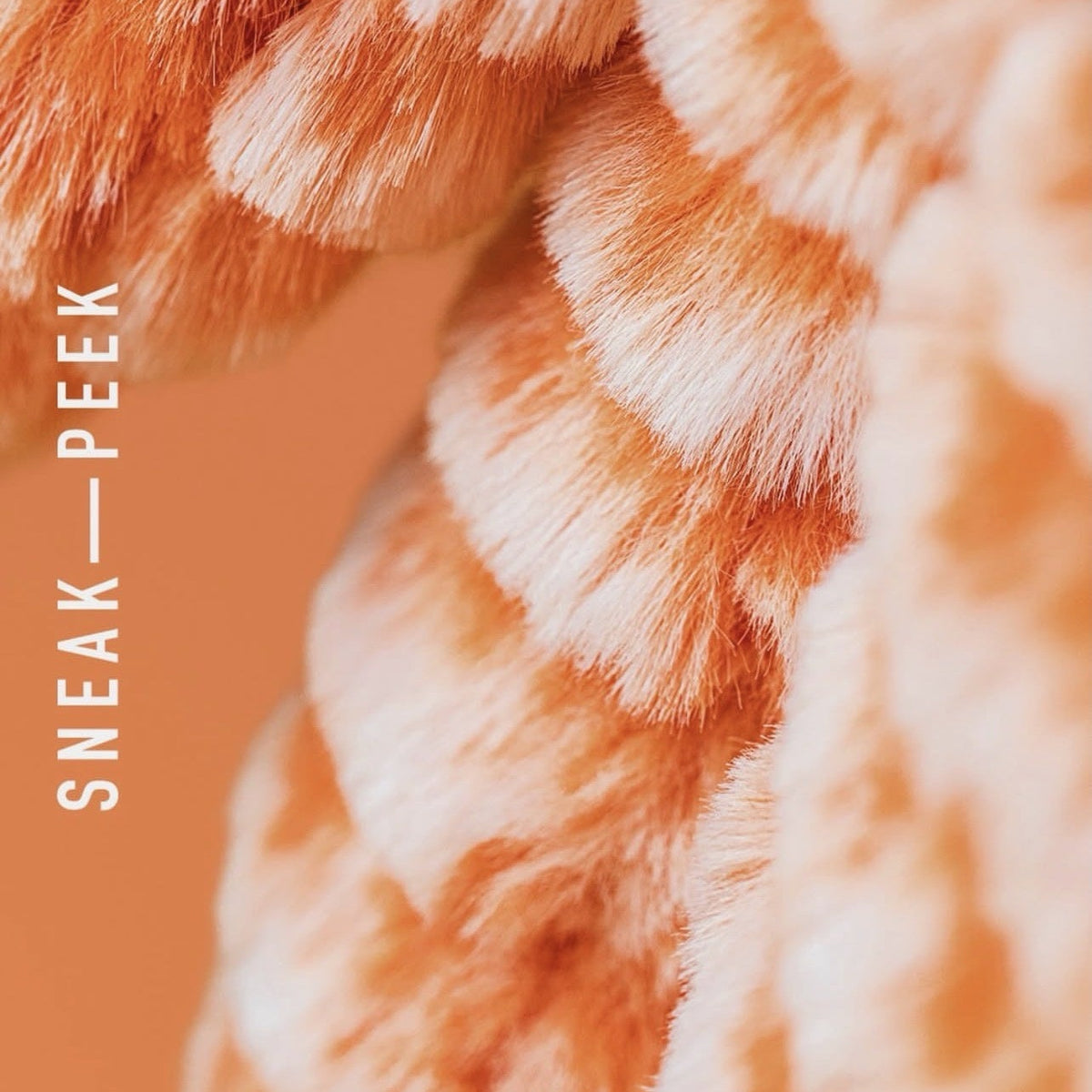 Close-up of a plush, ribbed faux-fur or knit textile in peach and cream tones, with vertical text reading 'SNEAK—PEEK' along the left side.