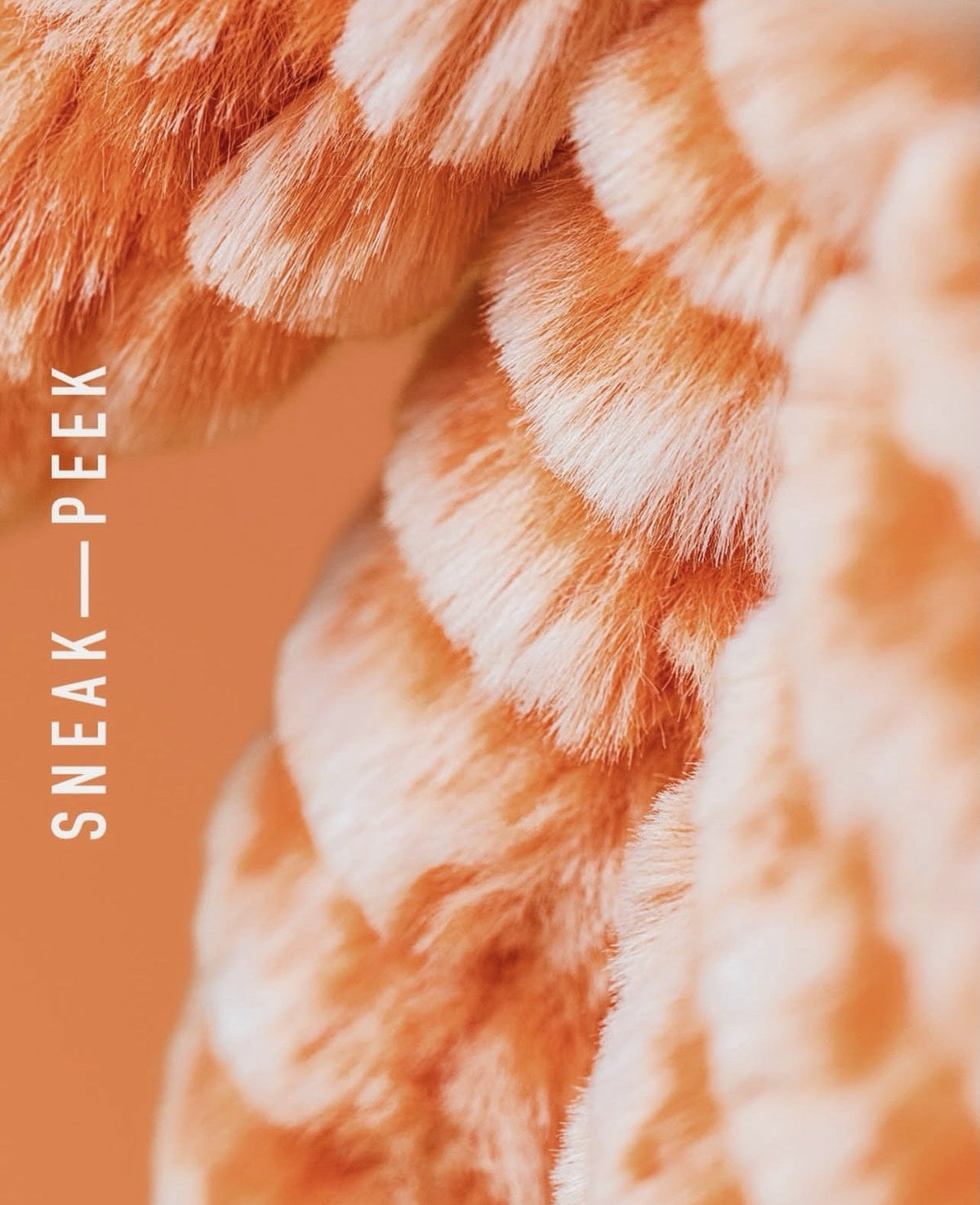 Close-up of a plush, ribbed faux-fur or knit textile in peach and cream tones, with vertical text reading 'SNEAK—PEEK' along the left side.