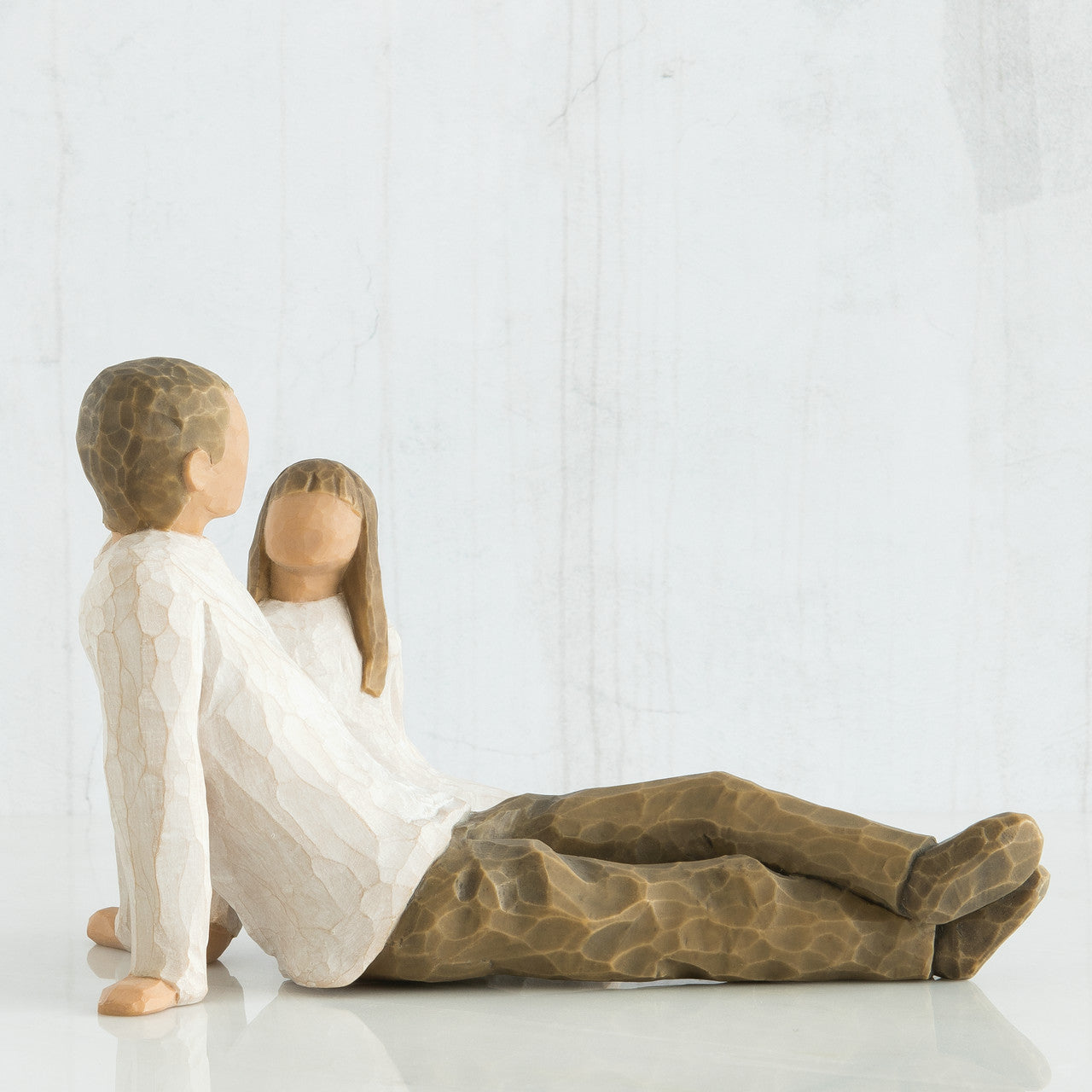 willow tree figures of a father and his daughter sitting on the floor against a white wall.
