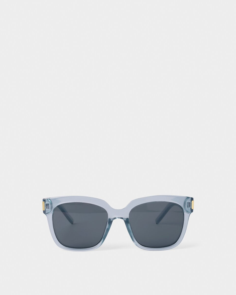 katie loxton roma Sunglasses with a clear frame and dark lenses on a white background