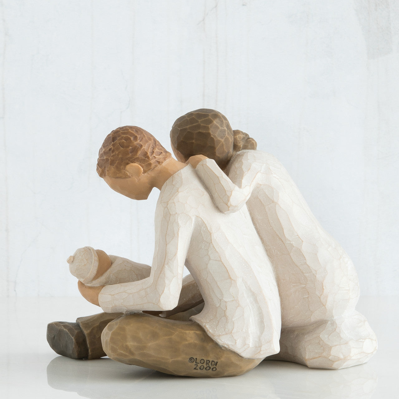 Willow tree sculpture of a father, mother and child embracing on a white background