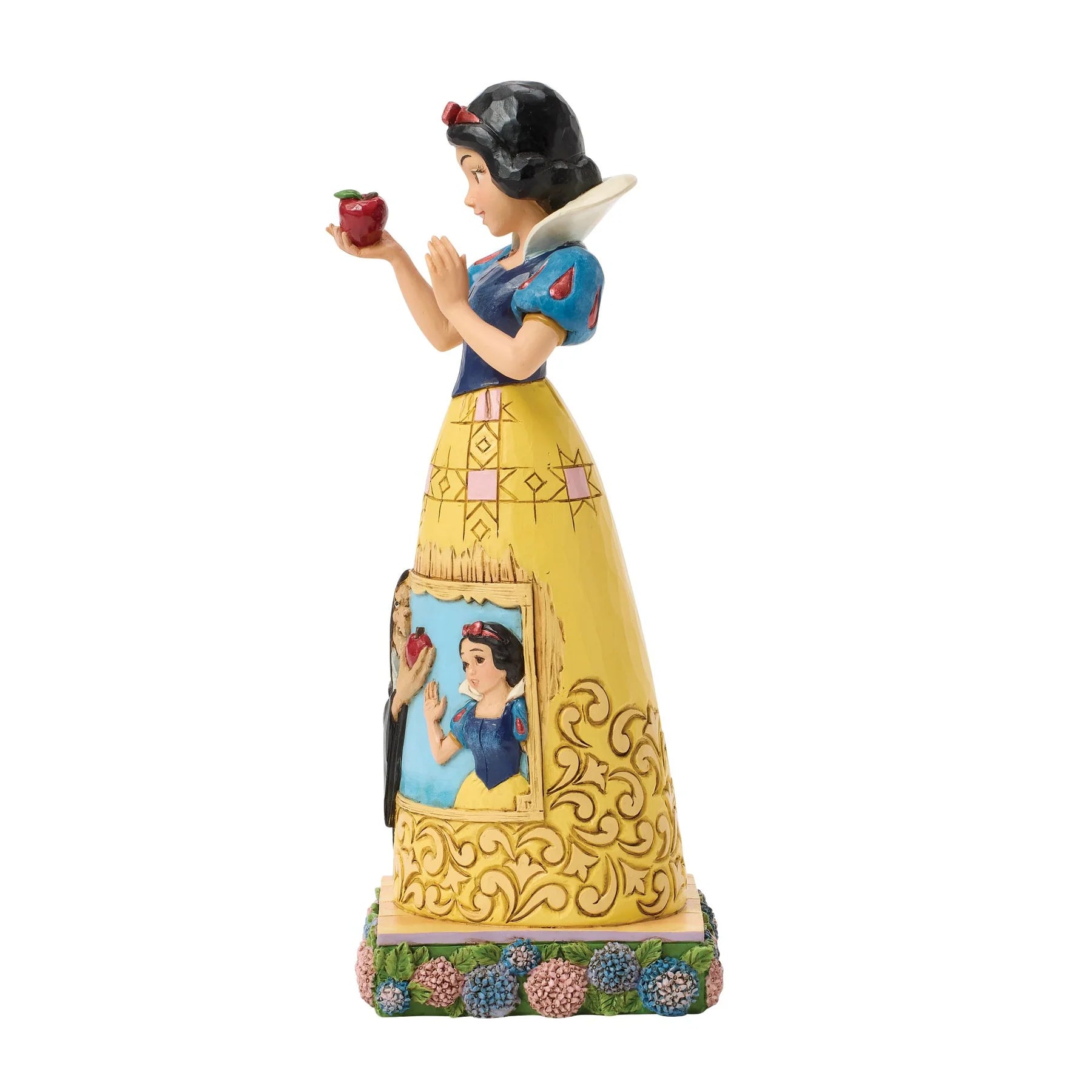 A Snow White figurine holding a red apple, standing on a decorative base with floral accents. The figure is dressed in a yellow skirt with blue bodice details and a portrait panel on the front.