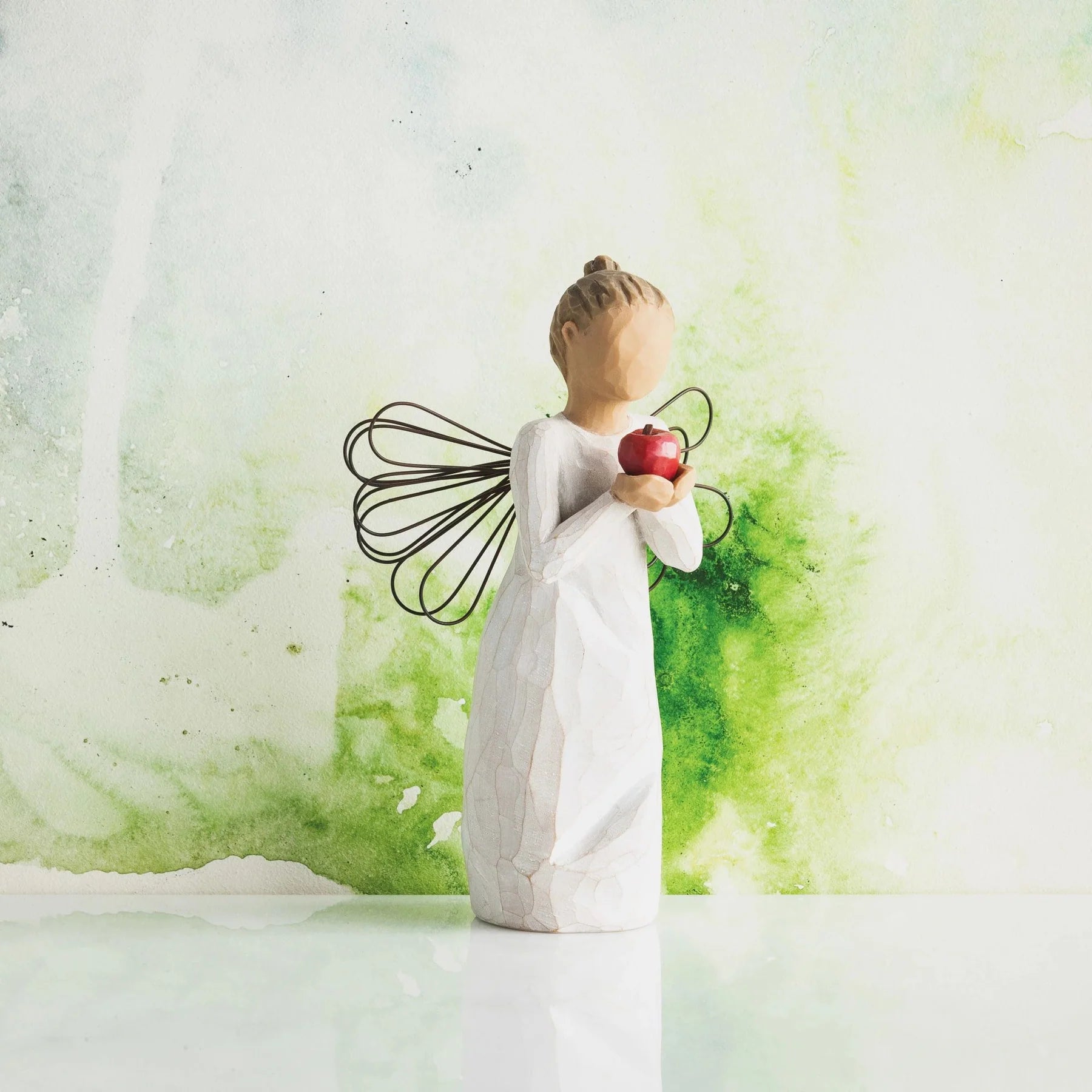 willow tree angel of a figure holding an apple against a green and white abstract background