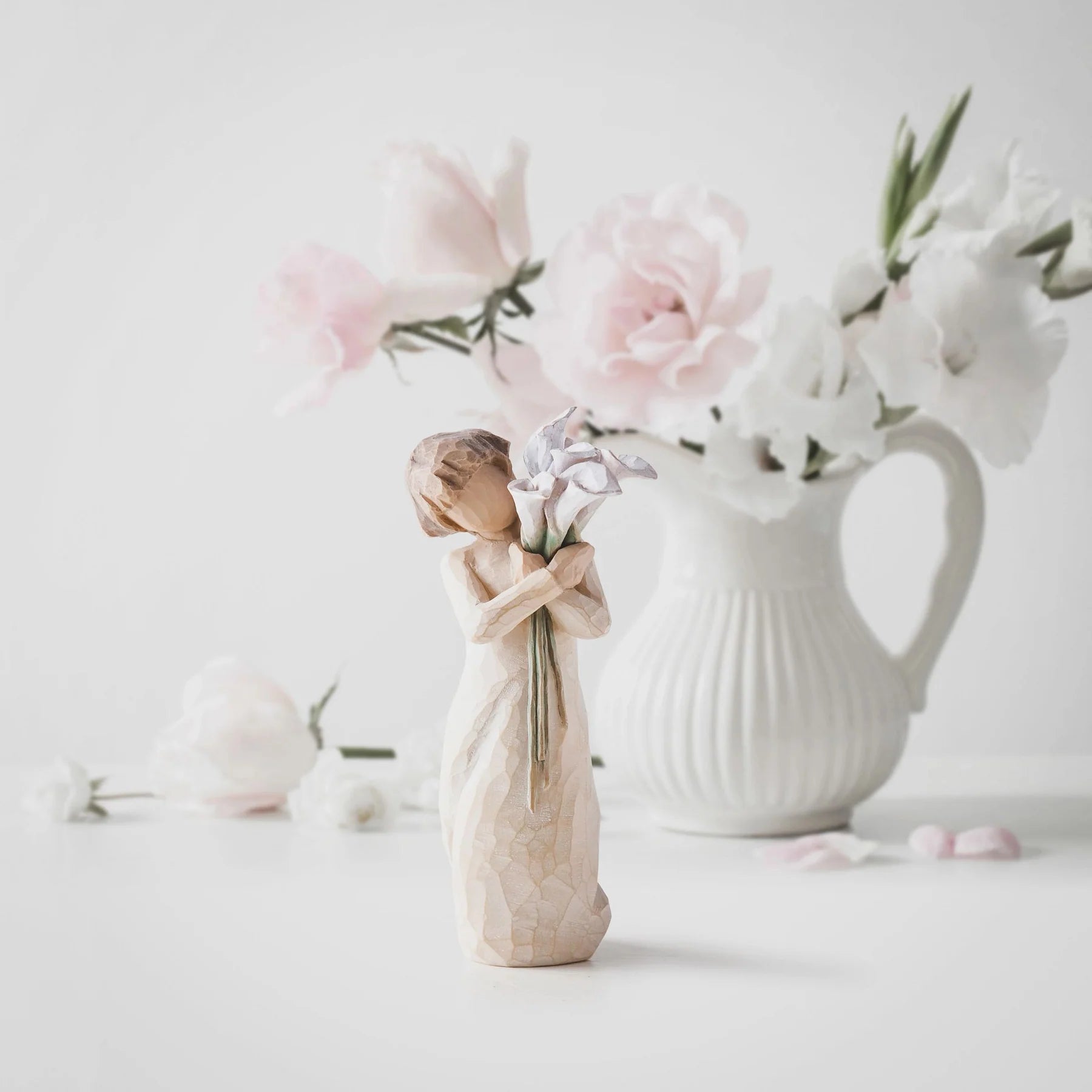 willow tree beautiful wishes figurine holding a vase with flowers in front of a larger vase with pink flowers on a light back ground