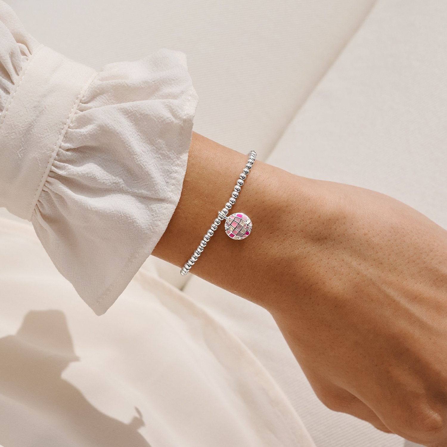 Bracelet with a pink and silver Glitterball charm on a wrist against a neutral background