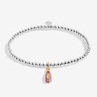 A silver beaded stretch bracelet with a dangling pink Champagne bottle charm featuring gold detailing, shown on a light white background.