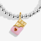 A close-up of a silver beaded Joma Jewellery featuring a charm shaped like a chocolate bar with gold detailing and a small red heart accent, set against a clean white background.