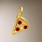 Close up image of Joma Jewellery pizza slice charm on a grey background.