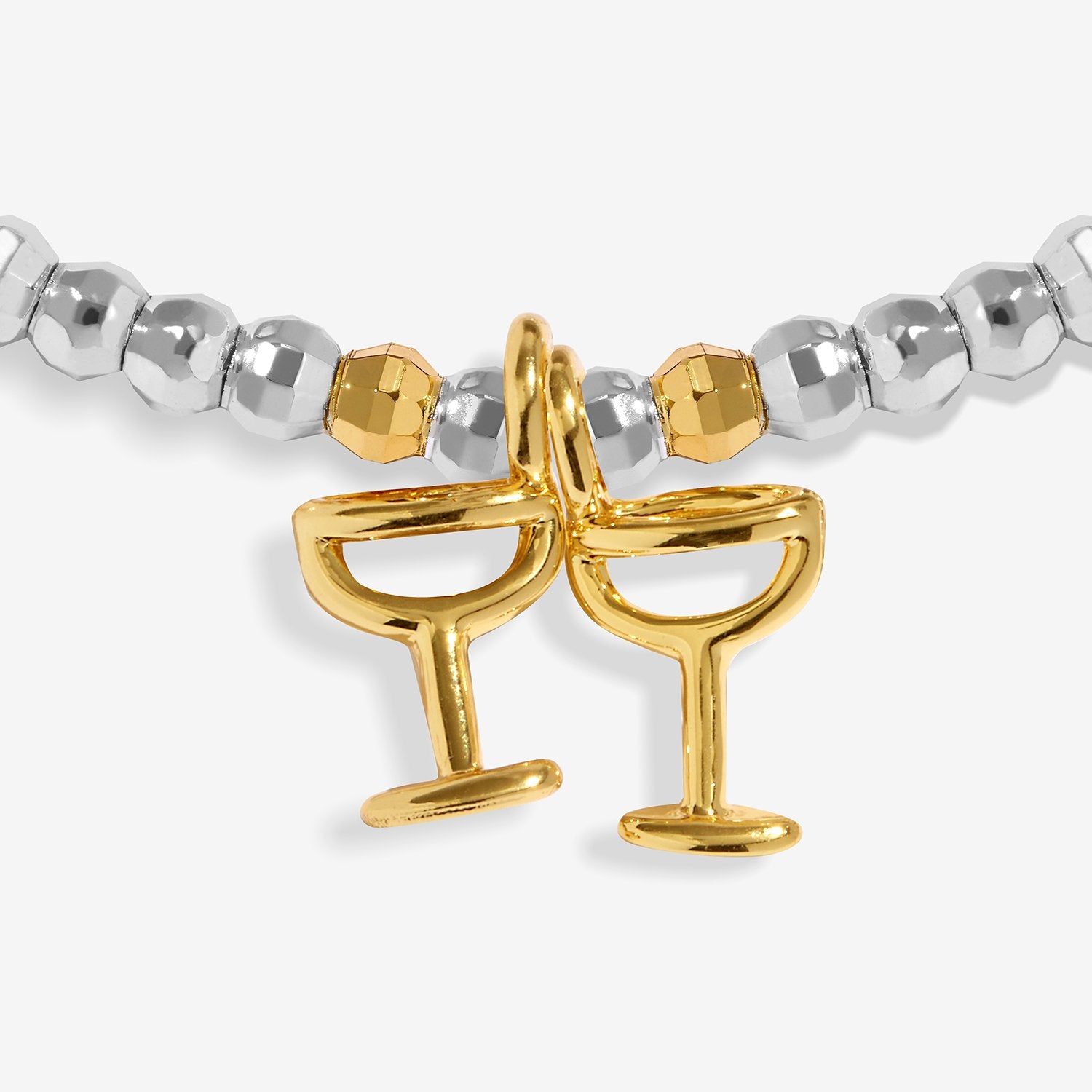 A close-up of Joma Jewellery beaded bracelet featuring silver faceted round beads, a small gold faceted bead, and two interlocking gold cocktail glass charms at the center, set against a light gray background.