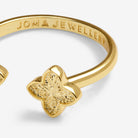 Gold clover-shaped ring with a textured center and 'JOMA JEWELLERY' engraved inside the band, shown on a light gray background.