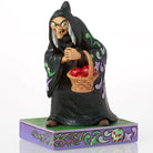 A decorative figurine of a witch in a black robe holding a basket of red apples, standing on a purple and green base with ornate scrollwork, photographed on a white background.