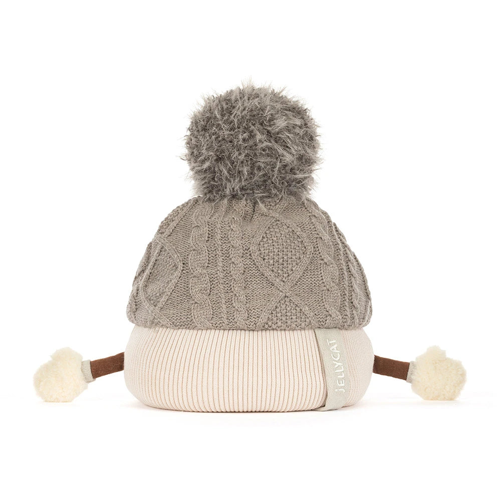 Jellycat amuseables pomilly hat with a gray cable-knit top, a cream ribbed bottom, a gray pom-pom, and small fabric hands and feet, shown on a white background. A side tag reads JELLYCAT.