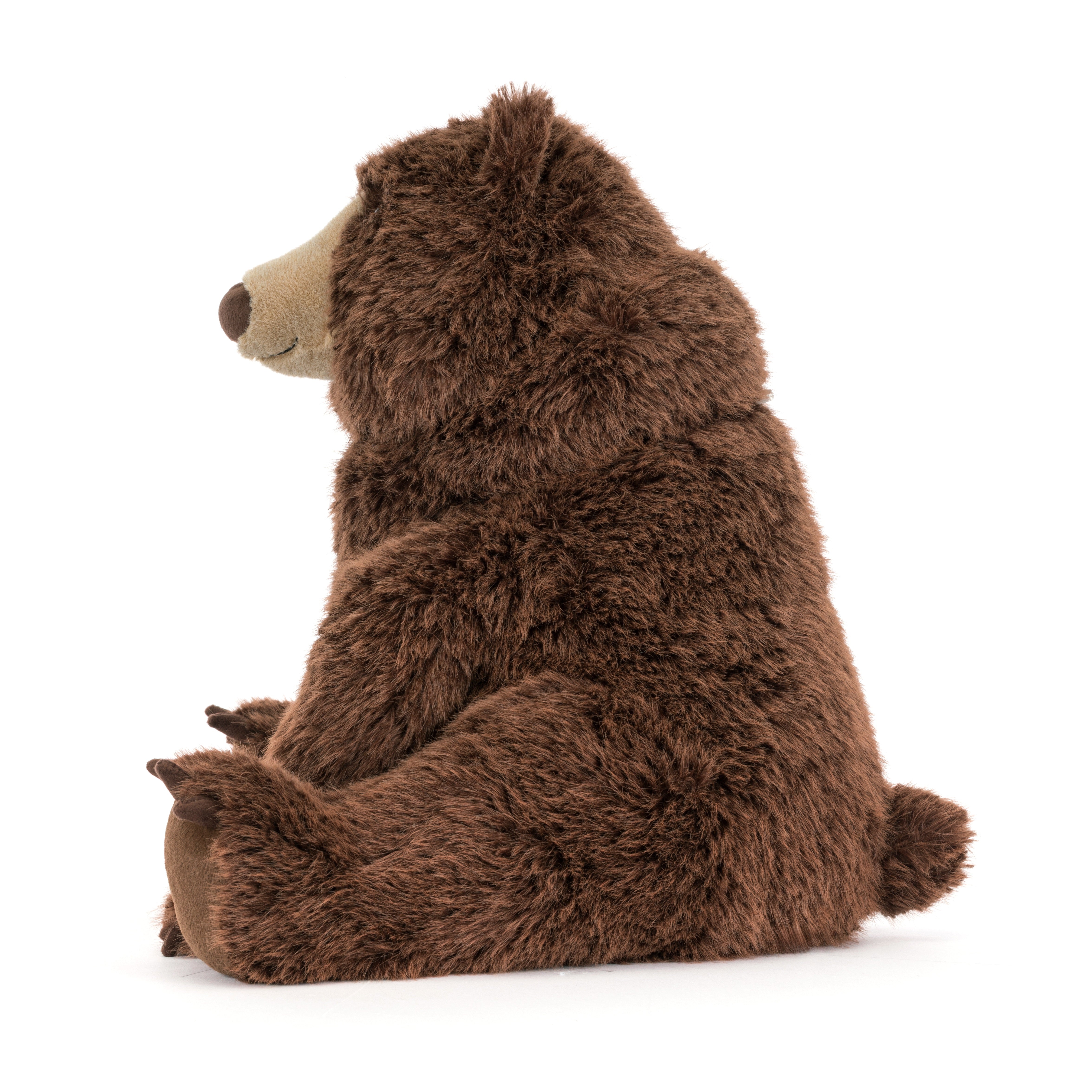 A plush brown bear toy sitting upright, photographed from the side against a clean white background.