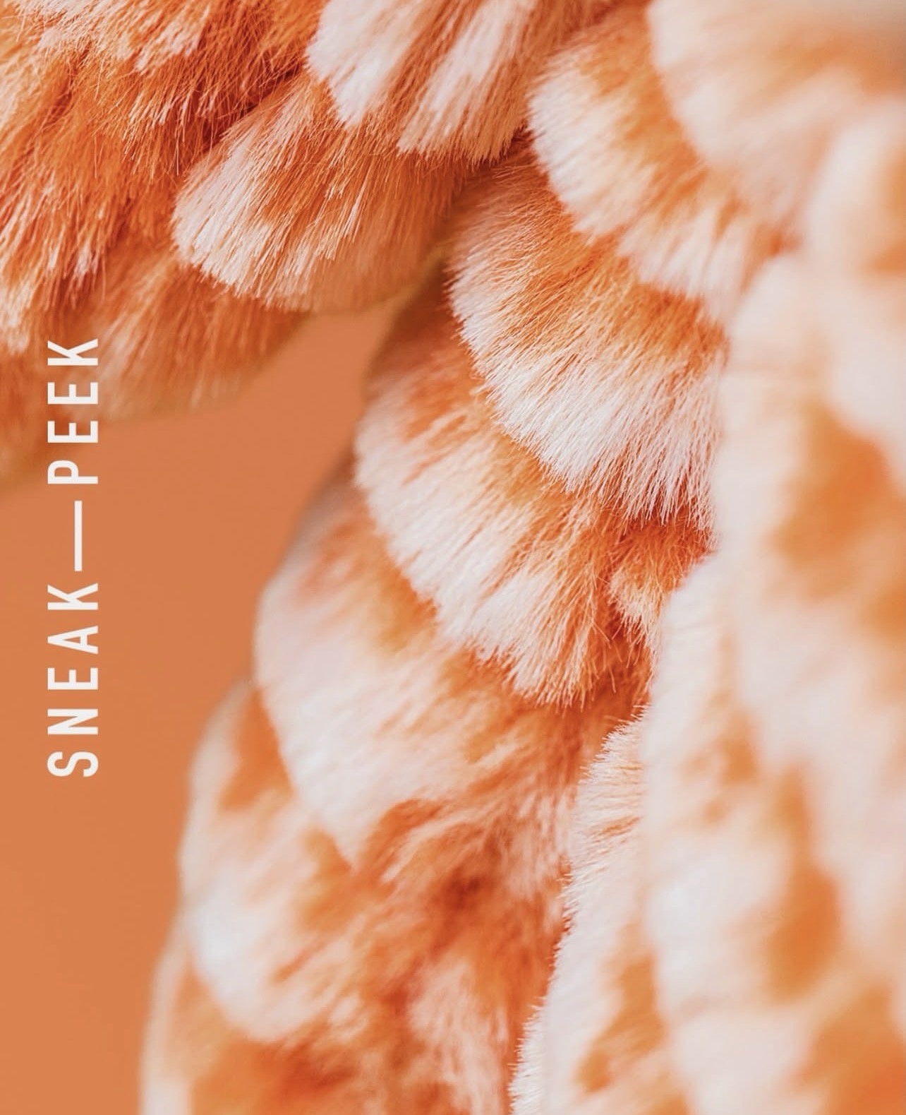 Close-up of a plush, ribbed faux-fur or knit textile in peach and cream tones, with vertical text reading 'SNEAK—PEEK' along the left side.