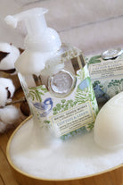 Cotton & Linen Michel Design Works Hand soap bottle with pump and packaging on a wooden surface with cotton flowers in the background