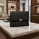 Katie Loxton black Lea clutch bag on a table in store