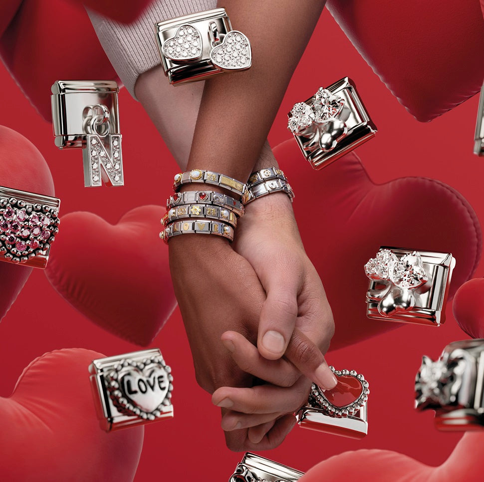 Nomination Italy image showing two hands holding each other with classic composable bracelets and various love themed charms on a red background
