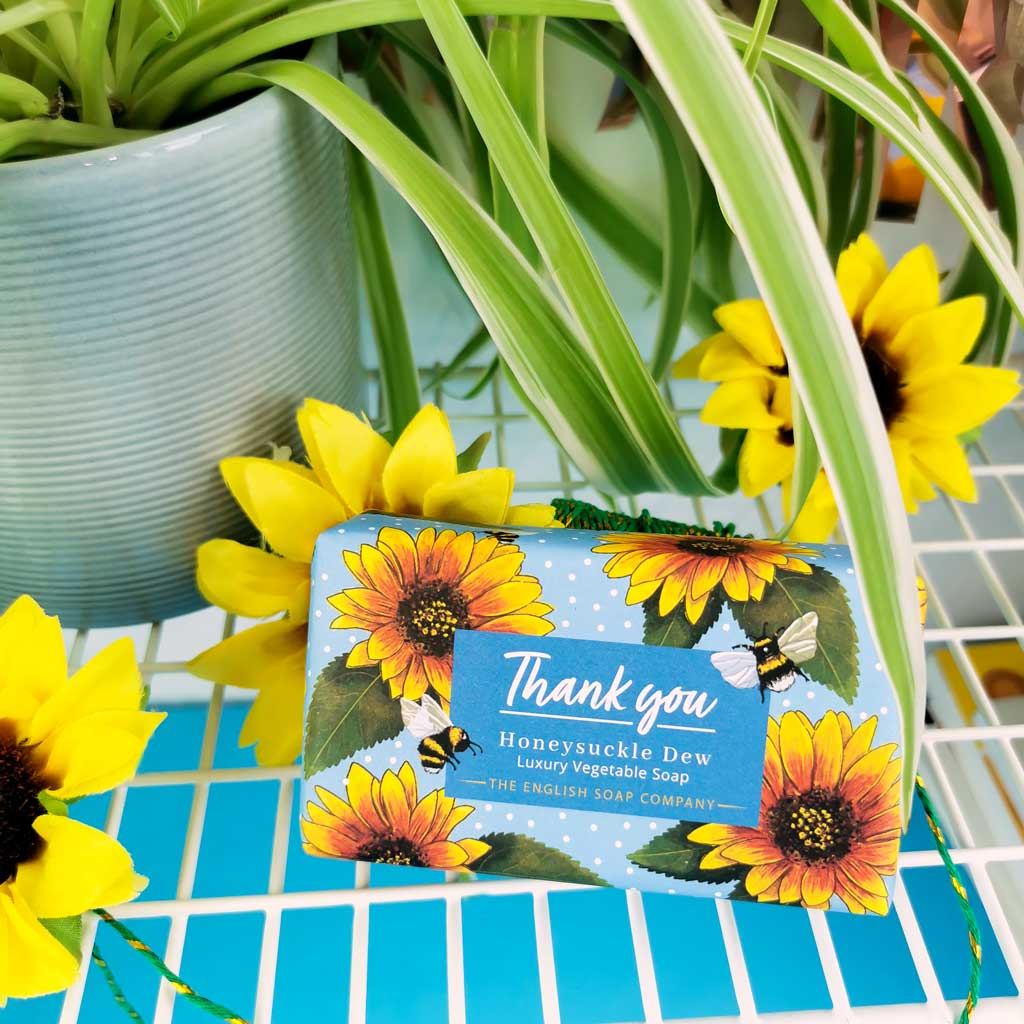 Soap bar with sunflower design and 'Thank you' text, surrounded by sunflowers and plants.
