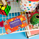 Colorful soap packaging with 'Happy Birthday' text on a blue surface with various items around.