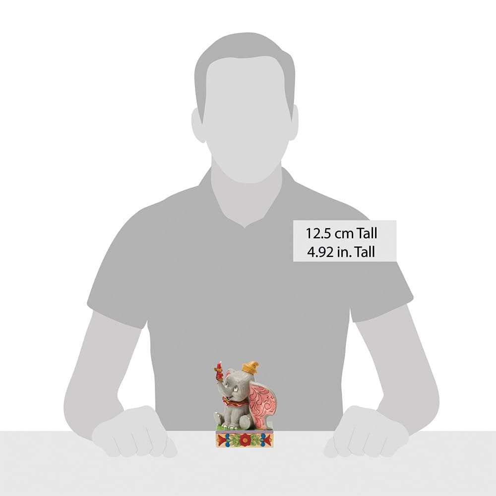 A small figurine of Dumbo the elephant wearing a yellow hat displayed in front of a gray silhouette of a person for scale. A text label indicates the height is 12.