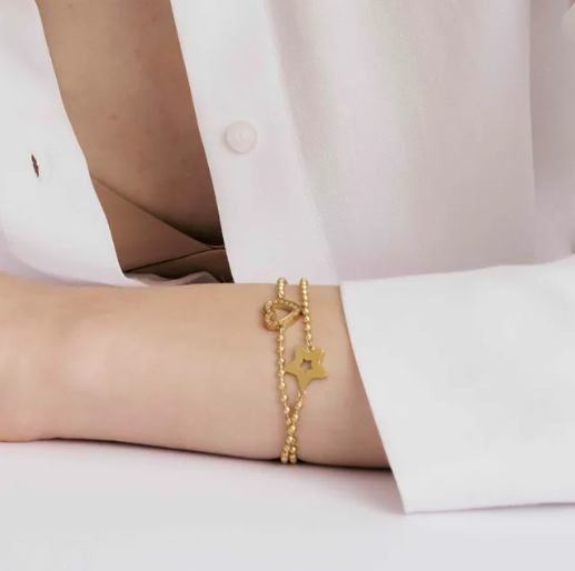 Nomination Italy Gold coloured bracelets. one with a star charm and one with  heart charm. On a person's wrist, wearing a white shirt.
