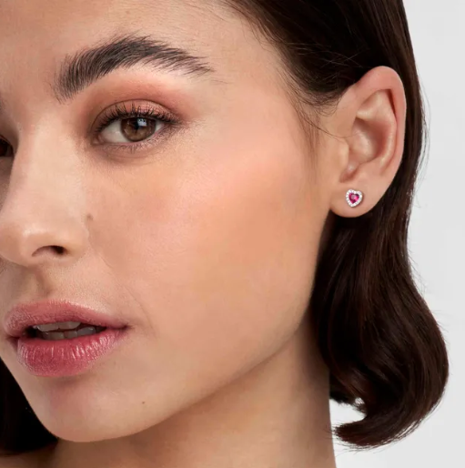 Close-up of a woman wearing a heart-shaped nomination earring studs on a plain background. From the all my love jewellery collection 