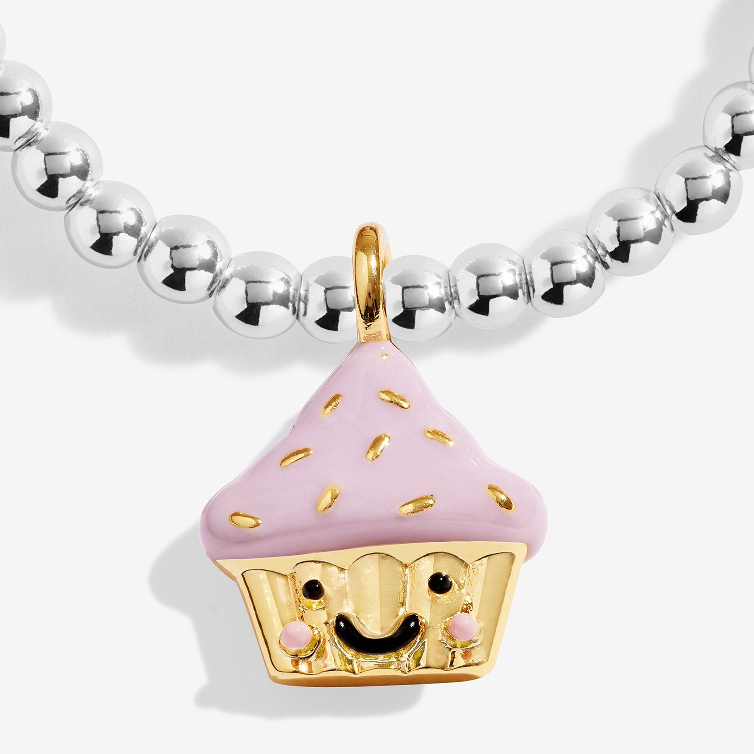 A close-up of a silver-plated beaded bracelet featuring a cute cupcake charm. The cupcake has a light pink frosting top with small gold sprinkles, a gold wrapper, and a smiling face with pink cheeks.