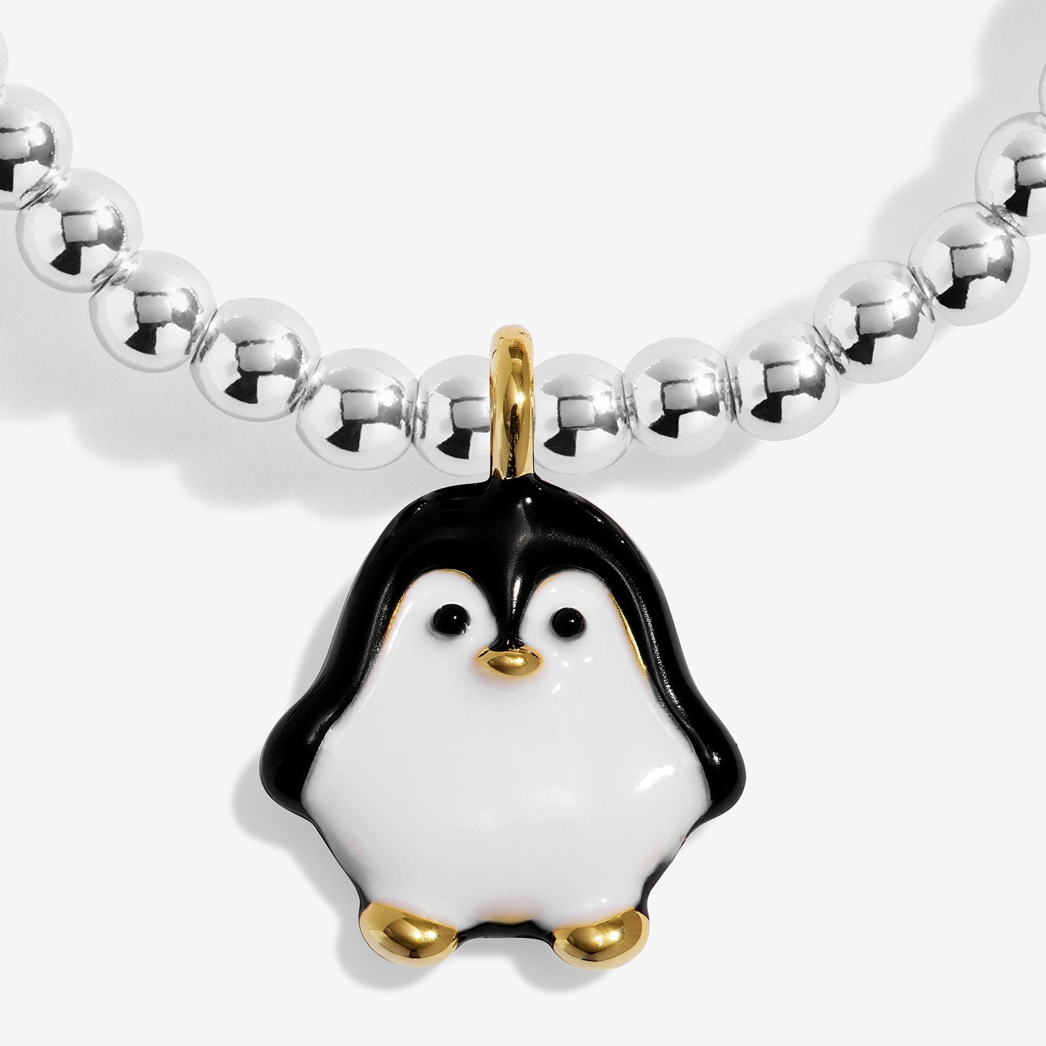 A close-up of a beaded silver-plated bracelet featuring a penguin charm. The bracelet has a strand of polished silver-colored round beads and a central penguin charm with a glossy white and black enamel body, accented by gold-tone details on the beak, feet, and top loop.