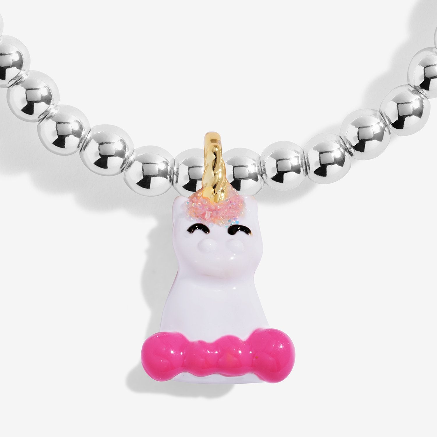 A close-up of a silver-plated beaded bracelet featuring a white unicorn pendant with a gold horn, pink glittery hair, and a pink bow.