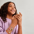 a child wearing multiple Jomee bracelets with colorful charms on a plain background