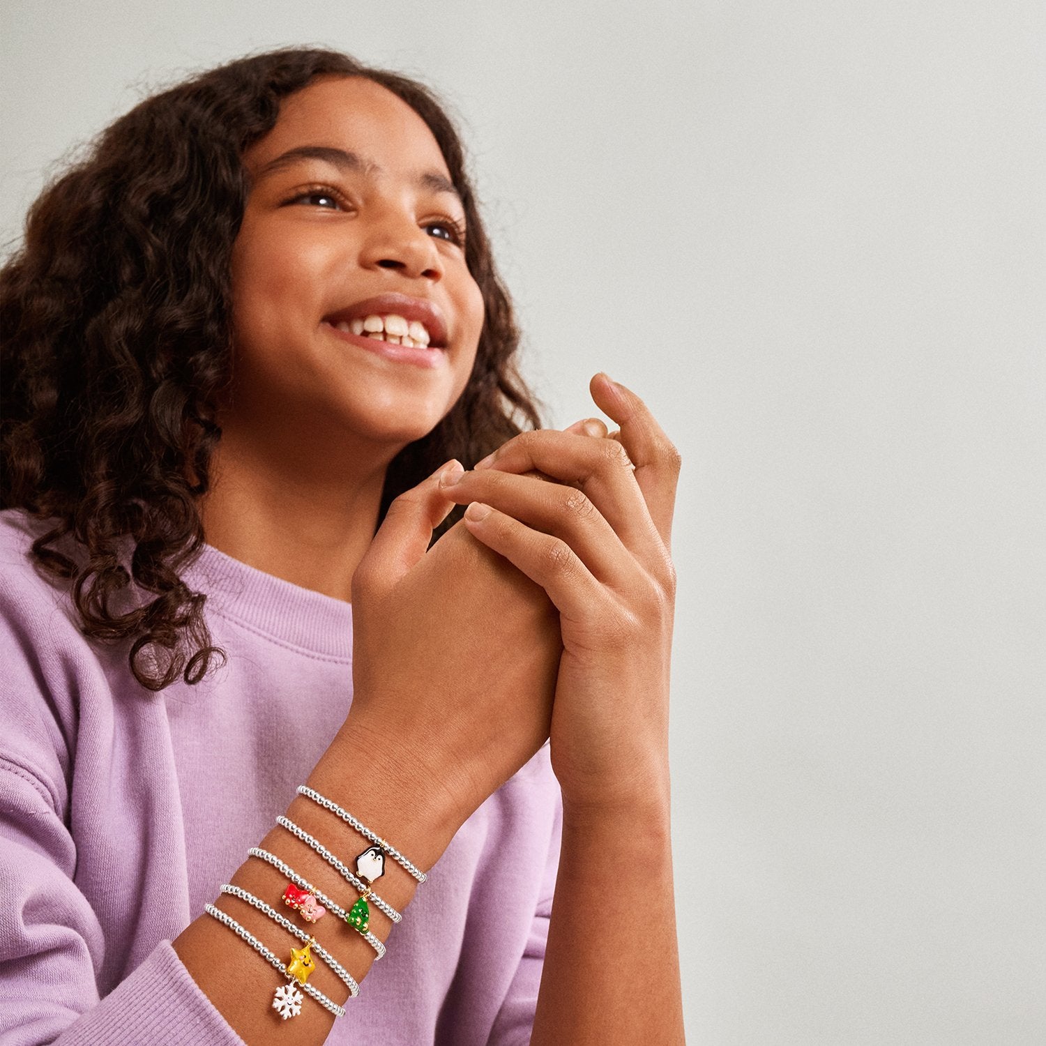 a child wearing multiple Jomee bracelets with colorful charms on a plain background