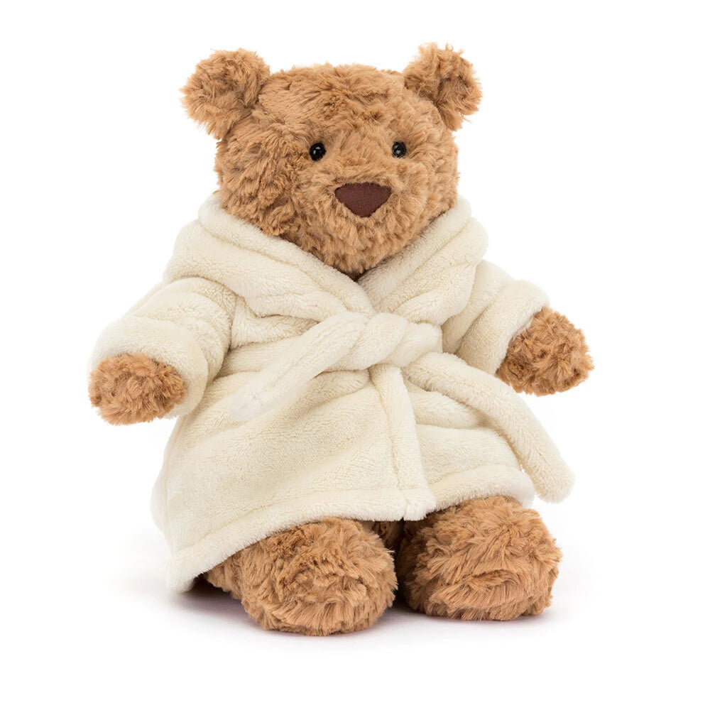 A brown plush jellycat Bartholomew teddy bear wearing a cream-colored plush bathrobe, photographed against a solid white background.