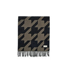 A folded woven scarf with a houndstooth pattern in black and taupe, featuring fringed edges and a small white brand label near the bottom right.