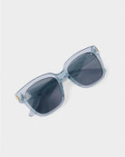 katie loxton roma Sunglasses with blue clear frame and dark lenses on a white background