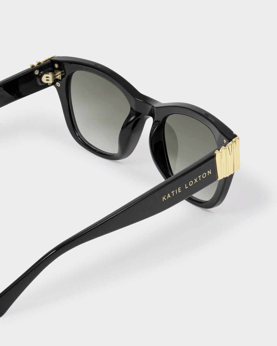 katie loxton seychelles Black sunglasses with gold accents on a white background