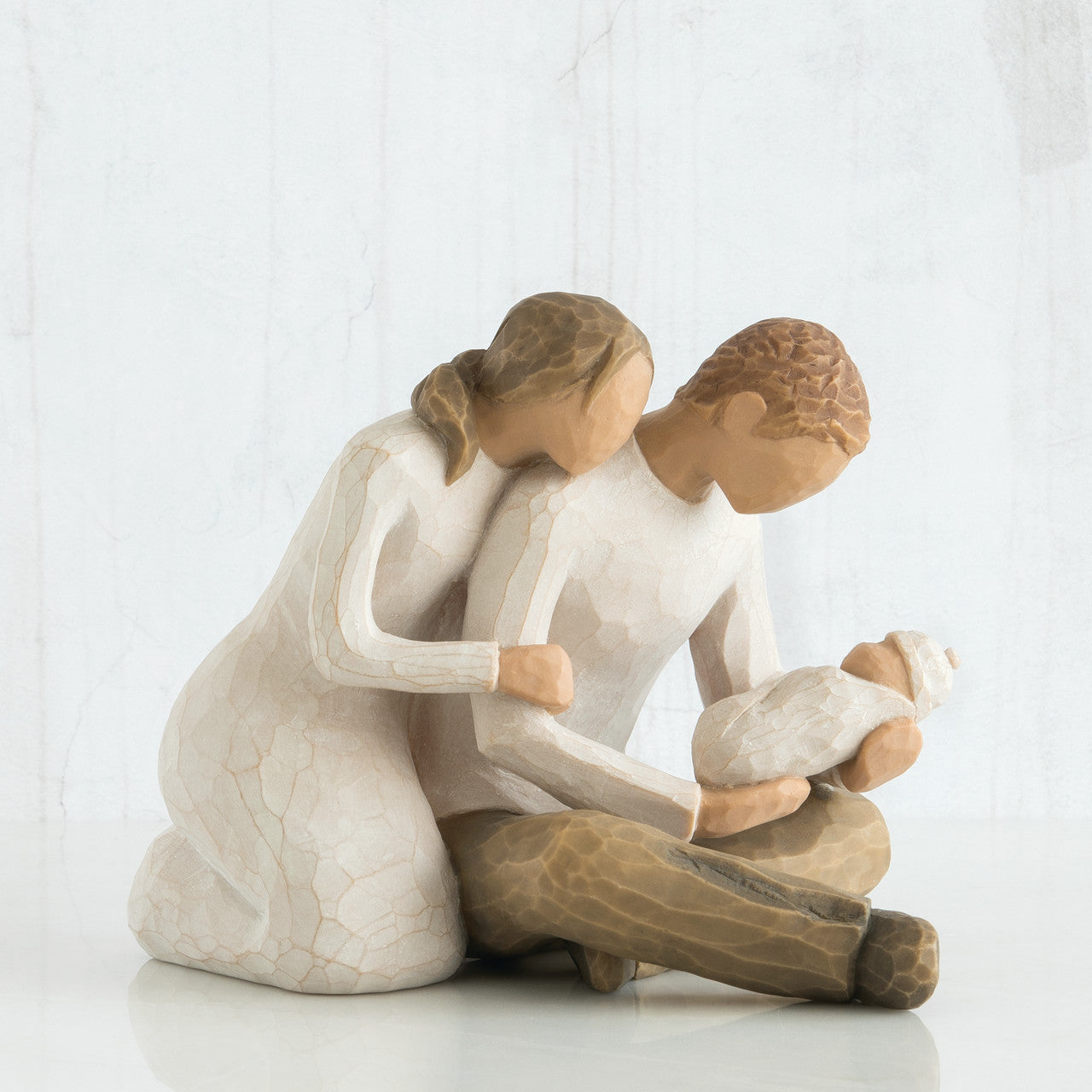willow tree Statue of a woman embracing a man while he holds a child on a white background