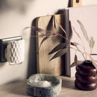 scent plug inserted into wall socket, surrounded by glassware and a vase on a surface with a neutral background.