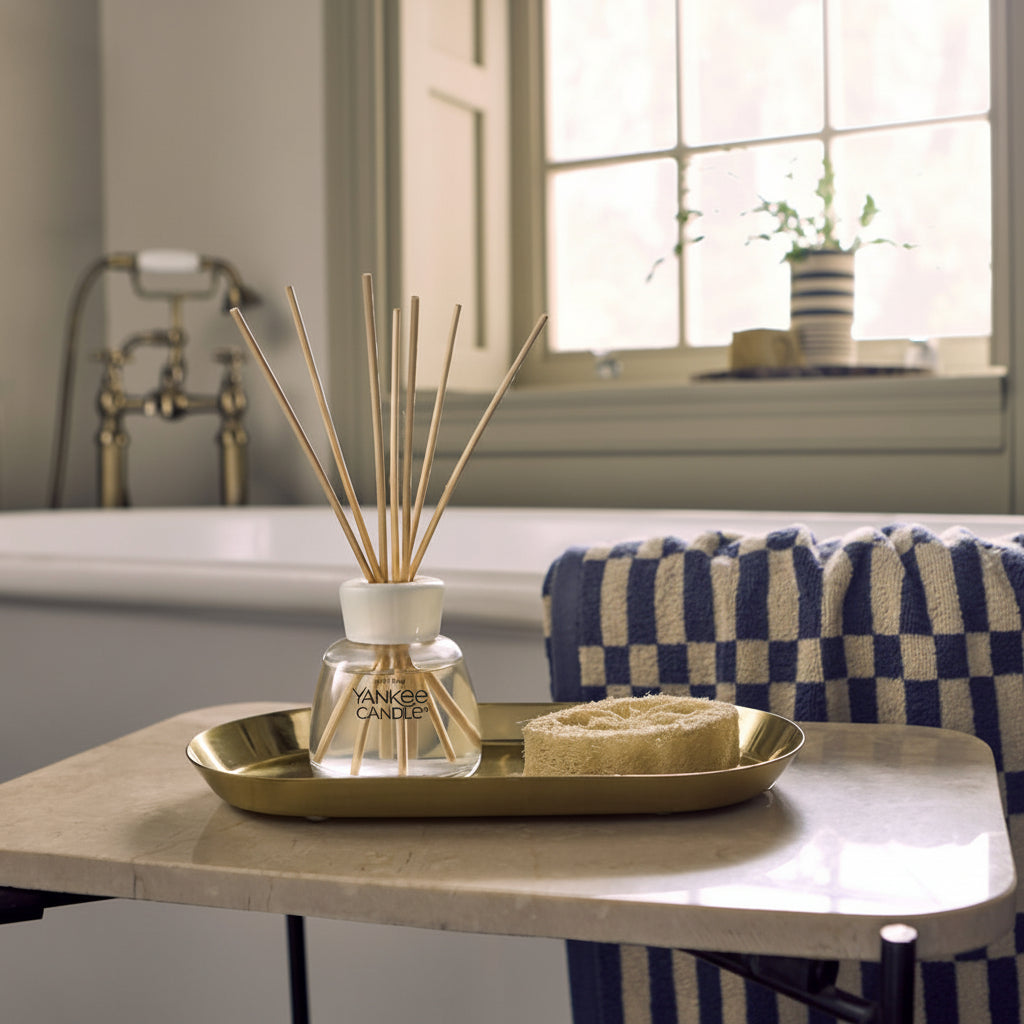 Bathroom setting with a bathtub, towel, and Yankee reed diffuser displayed on decorative tray.